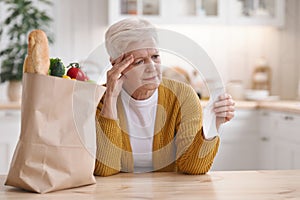 Upset elderly woman checking grocery check, kitchen interior