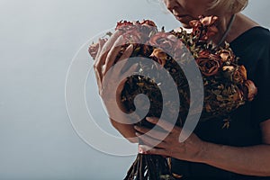 Upset elderly woman hold withered dry old rose flowers bouquet.