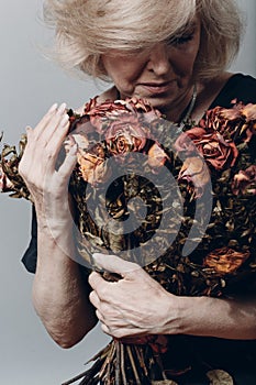 Upset elderly woman hold withered dry old rose flowers bouquet.