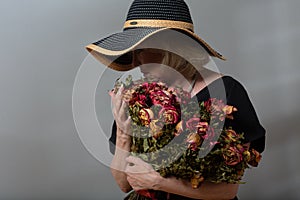 Upset elderly woman hold withered dry old rose flowers bouquet.