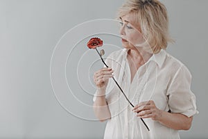 Upset elderly woman in white dressed hold withered one dry old rose flower.