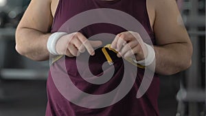 Upset fat man measuring belly with yellow tape, ineffective workout, overweight