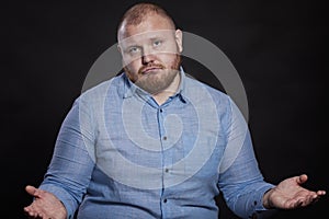 Upset fat red man with a beard spread his arms to the sides. Black background