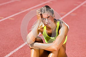 Upset female athlete sitting on running track