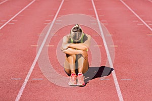 Upset female athlete sitting on running track