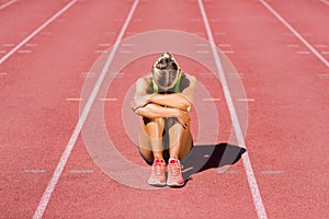 Upset female athlete sitting on running track photo