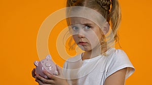 Upset female child shacking empty piggy bank, poor personal budget lack of money