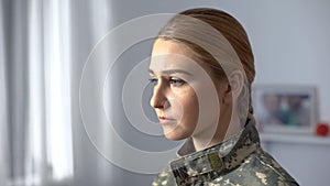 Upset female soldier in military uniform sadly looking in rehab center window