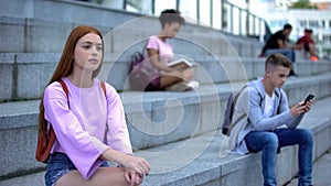 Upset female student sitting alone campus stairs, unsociable teenager problems photo