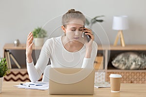 Upset female working ta laptop having unpleasant talk on phone