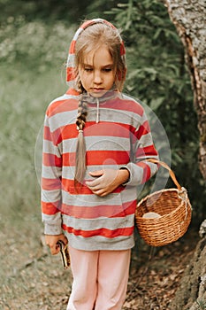 Upset or focused eight year old kid girl mushroom picker is seek for and picking mushrooms in the forest or woodland. child surviv