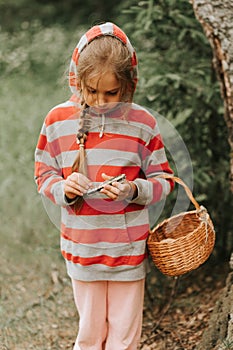 Upset or focused eight year old kid girl mushroom picker is seek for and picking mushrooms in the forest or woodland. child surviv