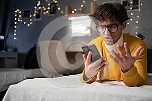 Upset frustrated male student reading bad news on message, having problem with device or Internet connection while lying