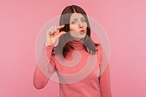 Upset frustrated woman with brown hair in pink sweater showing small size with her fingers, sceptic about centimeter inch size,