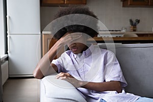 Upset fuzzy haired Black teen guy sitting on couch