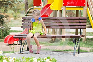 Upset girl bit her lip while sitting on bench on the background of the playground