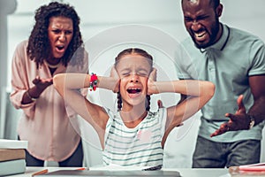 Upset girl closing ears while her parents yelling at her.