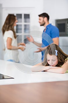 Upset girl leaning on table against parents