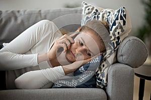 Upset girl lying on couch having unpleasant phone talk photo