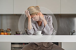Upset girl in morning pajama with bad mood drink coffee in kitchen. Depressed woman in the kitchen in the morning