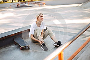 Upset girl sadly closing eyes holding her painful leg with skateboard near at skatepark isolated