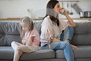 Upset girl sitting back to back with disappointed mother.