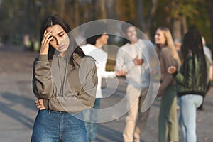 Upset girl staying apart from group of teenagers