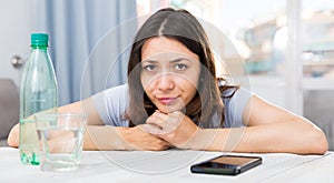 Upset girl suffering from troubles at table with bottled water