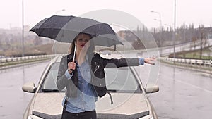 A upset girl with an umbrella catches a car standing on the road in the rain.