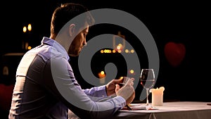 Upset handsome man looking at box with precious ring in restaurant, loneliness