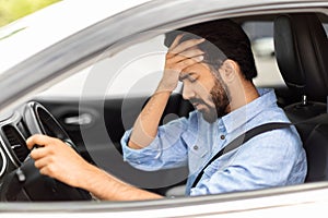 Upset indian driver sitting at front seat, touching his head