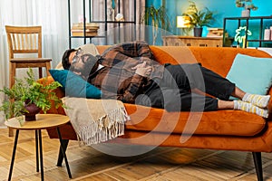 Upset Indian man lying on sofa feeling sudden strong abdominal stomach ache gastritis problem