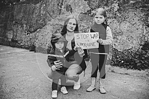 Upset kids with mother protesting war conflict raises banner with inscription message text Stop war in Ukraine. Crisis, peace,