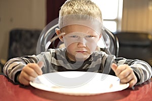 A Upset little boy waiting for dinner while holding a fork and a spoon