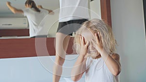 Upset little child with hyperactive mother jumping on bed on the background