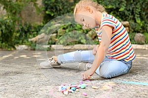 Upset little girl drawing with chalk on asphalt