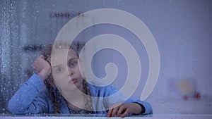 Upset little girl looking through window in rehabilitation center, therapy