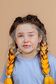 Upset little girl with open mouth and tears in eyes crying having kanekalon braids of yellow colour on head wearing