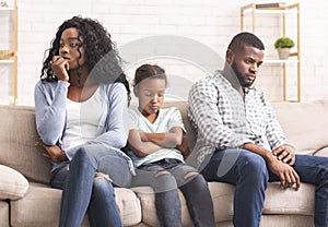 Upset little girl suffer from family conflict, sitting between parents.