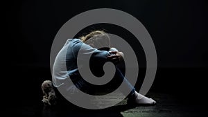 Upset little girl with teddy bear crying in dark abandoned room, loneliness