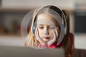 Upset Little Girl Wearing Wireless Headphones Looking At Laptop Screen