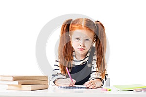 upset little schoolgirl drawing in notebook with felt tip pens and looking at camera