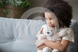 Upset lonely african kid girl holding teddy bear looking away