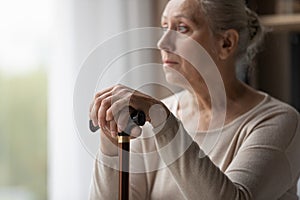 Upset lonely grey-haired older woman holds walking stick