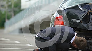 Upset male driver looking at car damage after back car crash at parking lot