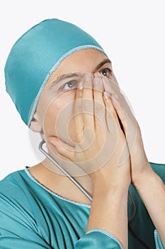 An upset male surgeon in scrubs looking up against white background