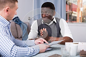 Upset man with friend looking worriedly at papers at home