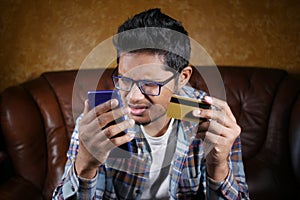 upset man holding credit card and smart phone while sited on sofa