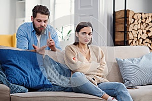 Upset man at table and woman with shopping bags in room. Money problems in relationship