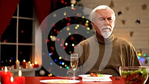 Upset man sitting on Christmas table alone, no mood for celebration holiday